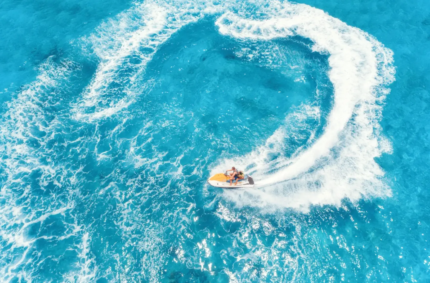 Aerial view of a jet ski carving a white arc across bright blue water