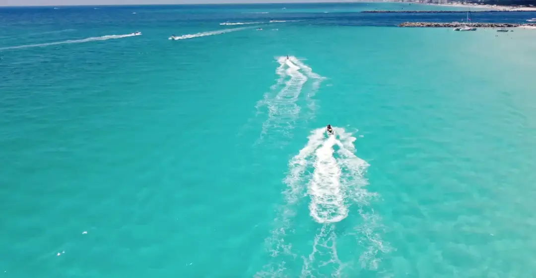 Aerial view of two jet skis drawing white wakes over bright turquoise shallows