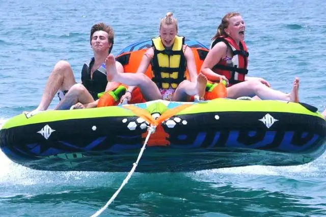 Three riders in life vests on an inflatable donut towed across the water